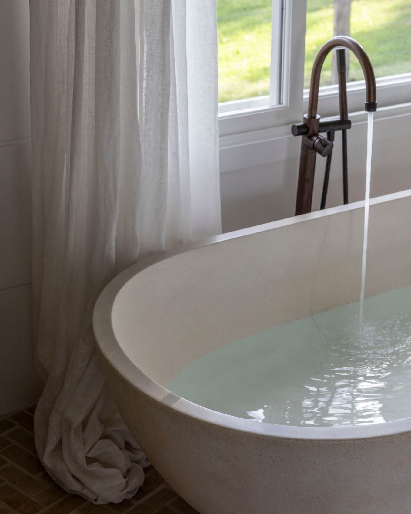 Le Viti Barn Newrybar: Curved stone bathtub with standalone bath spout, framed by lush linen curtains