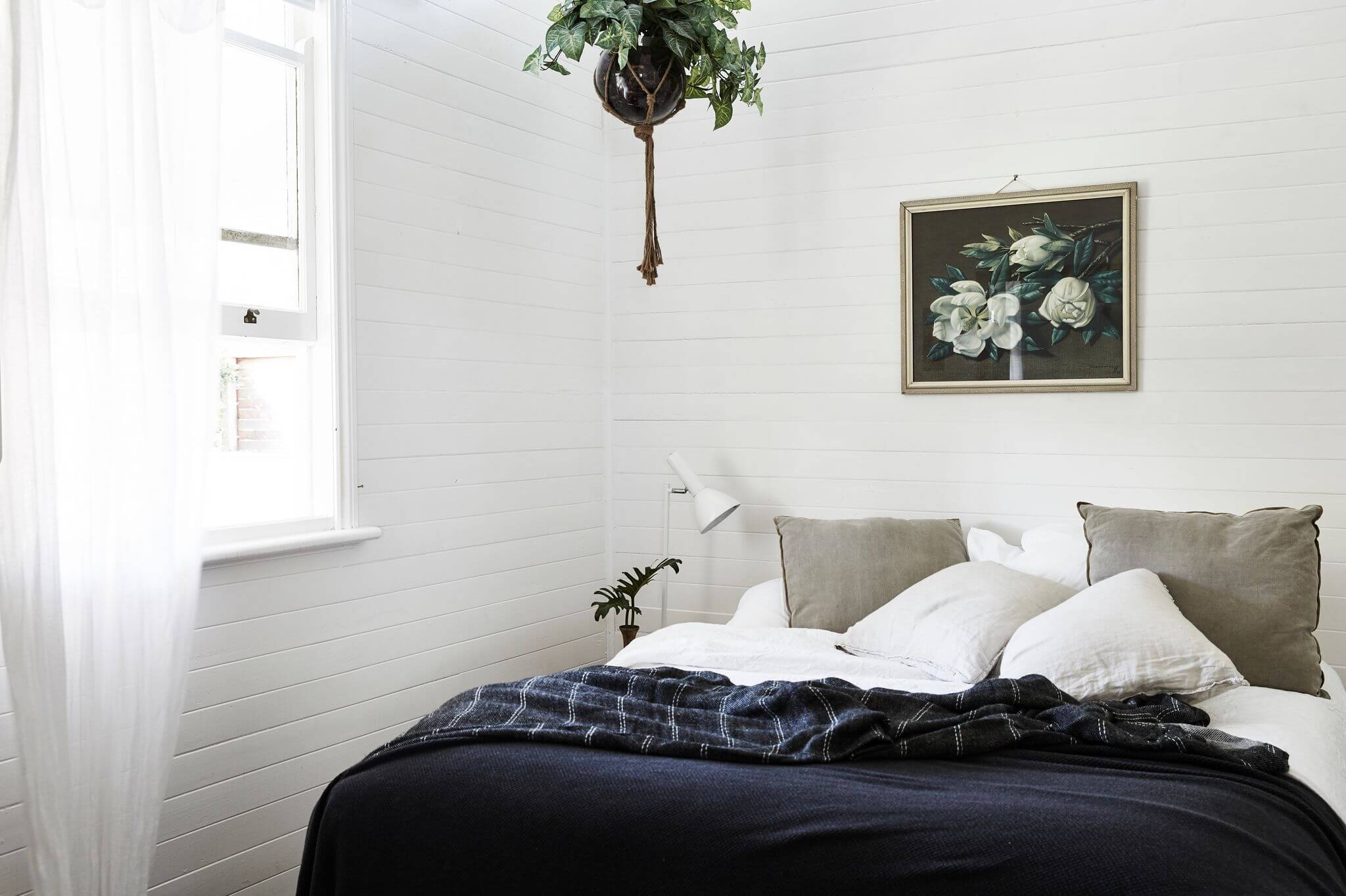 Layers of linen, antique art and a statement hanging plant in the bedroom at The Cottage, Byron Beach Abodes