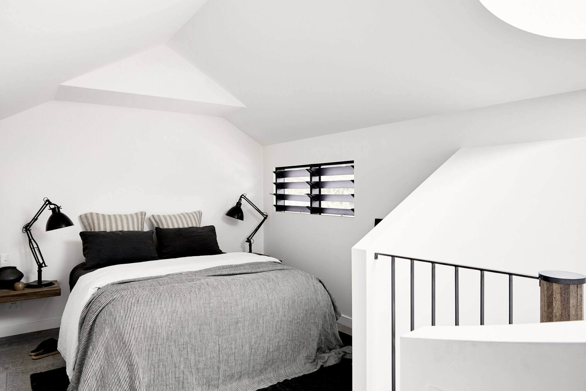 Loft bedroom at The Cabin, Byron Beach Abodes with pitched ceiling, white walls and luxury linen bedding