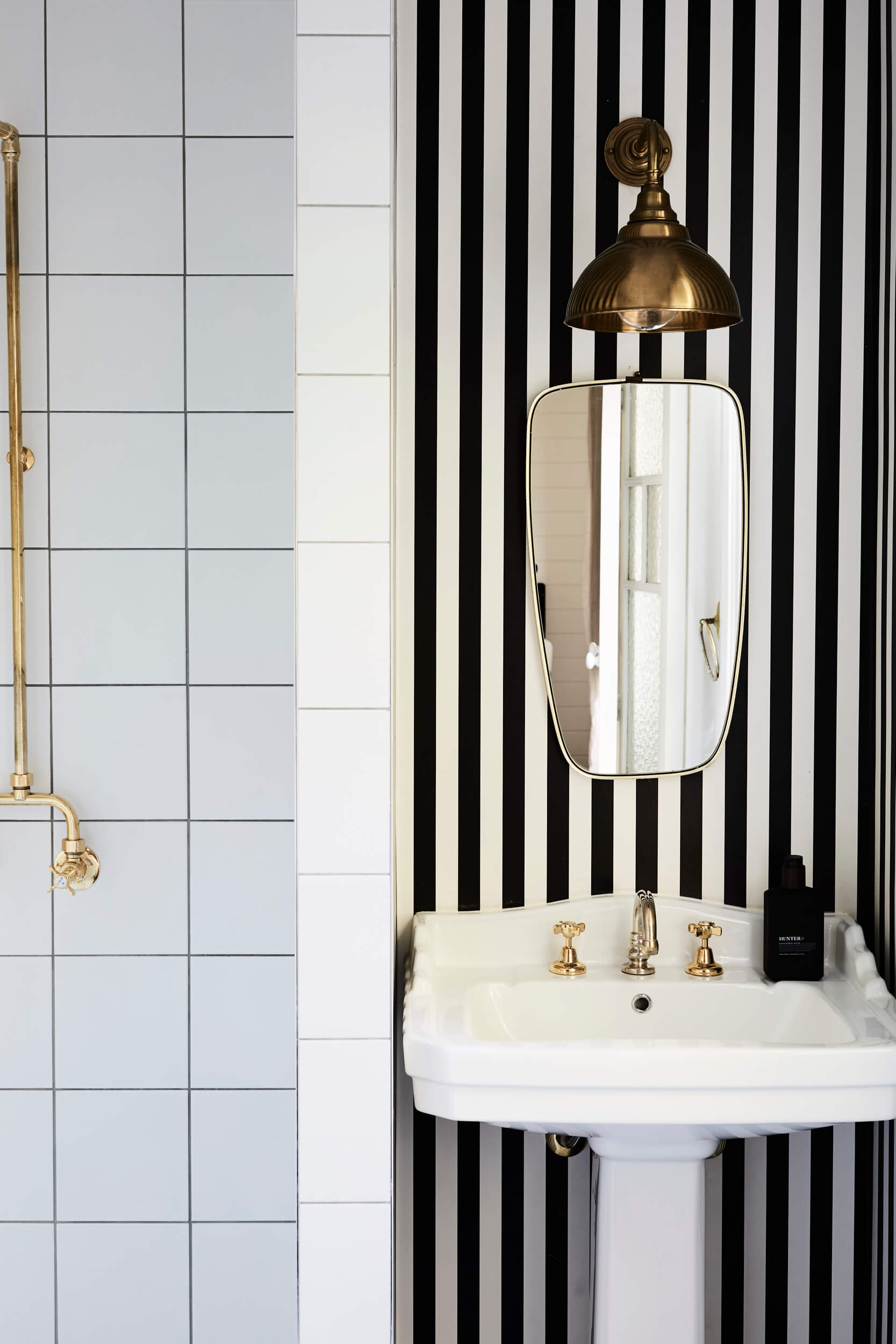 Ensuite at The Bower Cottage, The Bower Byron Bay with bold black and white striped wallpaper, vintage pedestal basin and brass fittings