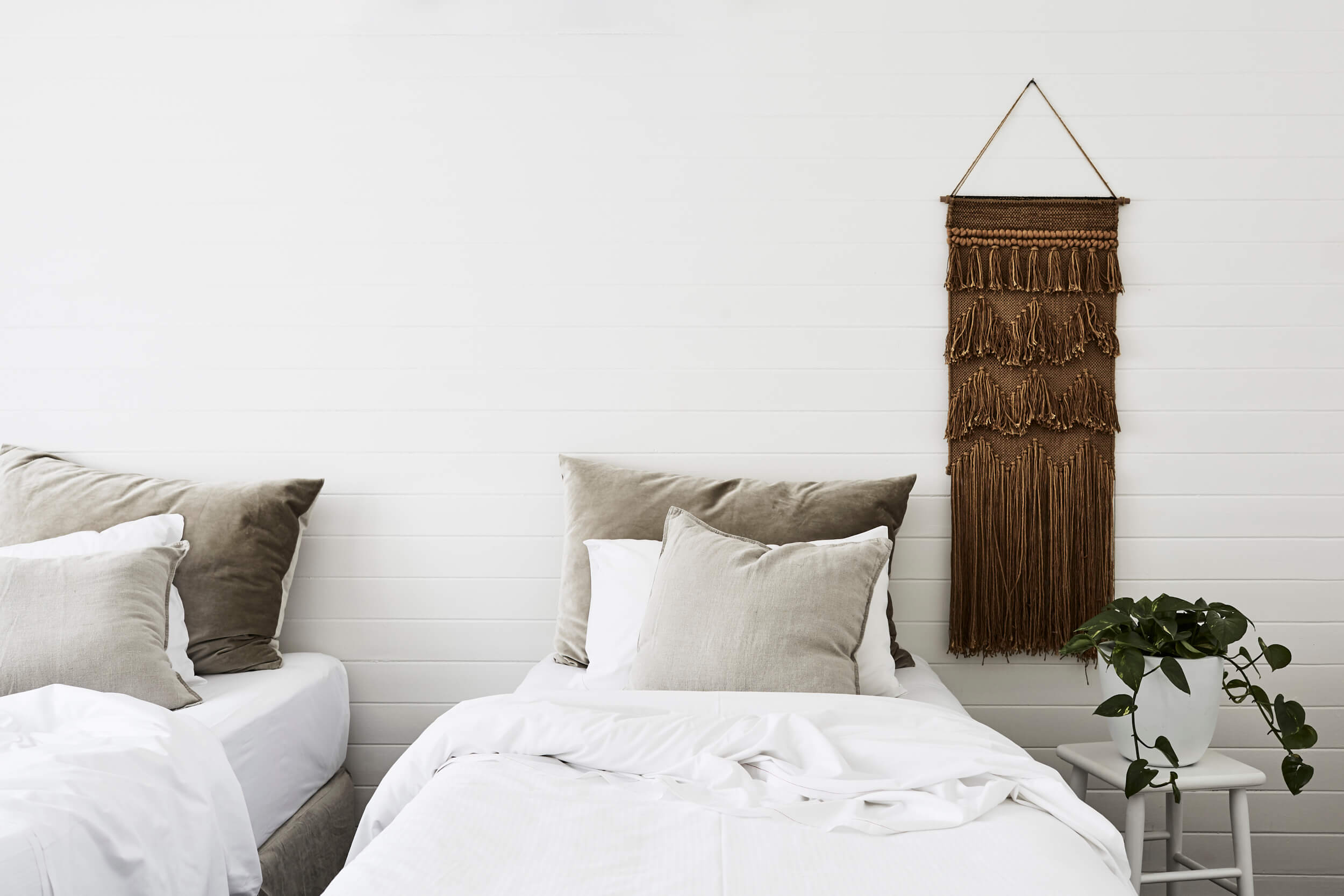 Bedroom at The Cottage, The Bower Byron Bay with woven wall hanging and beds with muted colour linens