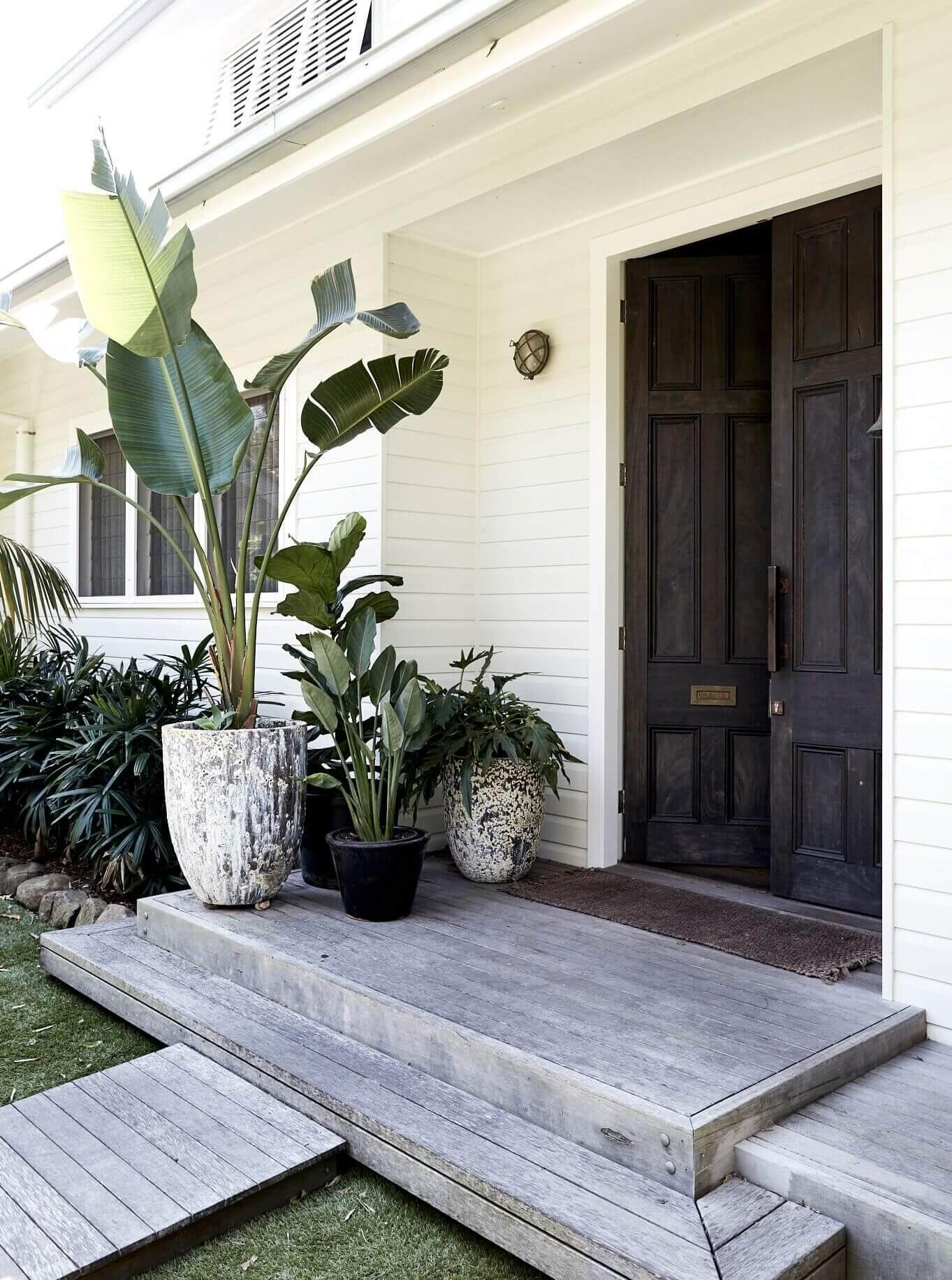 Entry to Magnolia House, Byron Beach Abodes with grey timber decking, large feature plants and recycled timber doors salvaged from the QVB in Sydney