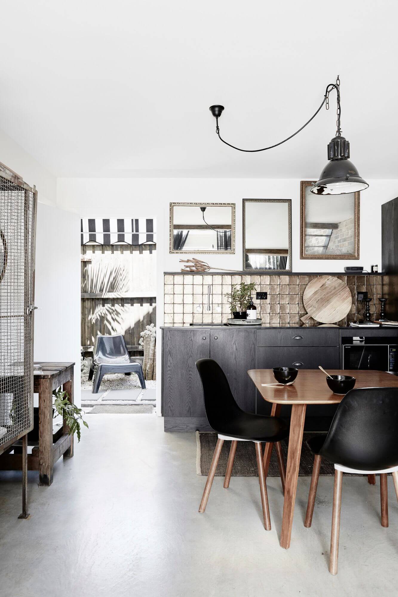 Quaint kitchenette at The Chapel, Byron Beach Abodes with handmade gold splashback tiles, black joinery, industrial pendant light and vintage timber table